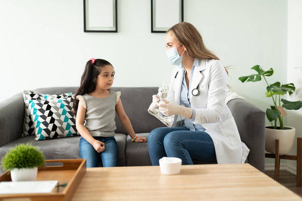 Жінка-лікар готує вакцину для маленької дівчинки і розмовляє з нею, щоб вона почувалася менш нервовою
 - Фото, зображення
