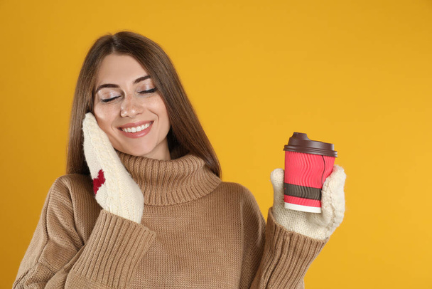 Happy beautiful woman with paper cup of mulled wine on yellow background - Photo, Image