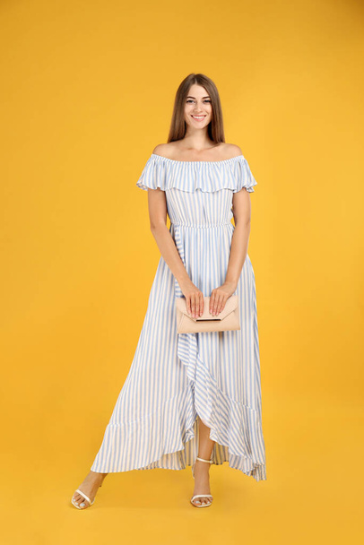 Young woman wearing stylish dress with elegant clutch on yellow background - Foto, immagini