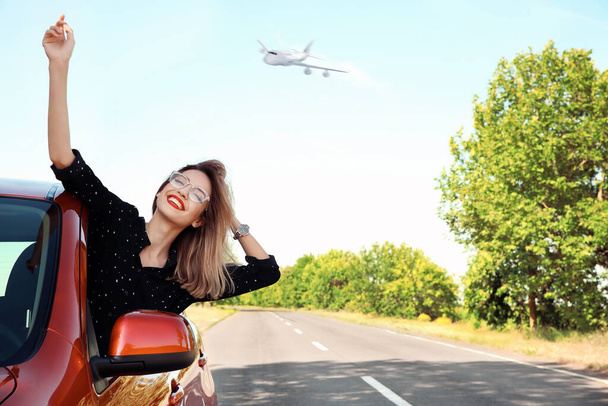 Young woman leaning out of car window and airplane in sky. Summer vacation - Foto, Imagem