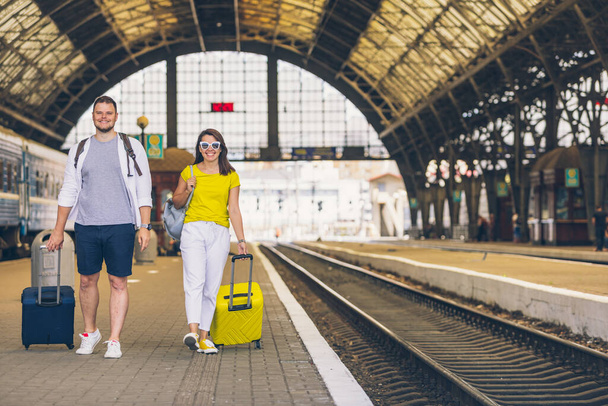 mladý pár chůze u vlakového nádraží s kufry na kolečkách pojetí cestování - Fotografie, Obrázek