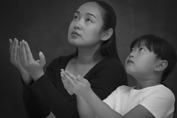 アジアの顔の女性と子供の祈りと神への崇拝宗教的信念で祈るために手を使用し、教会や中と黒の背景の一般的な場所でクリスチャンを崇拝 - 写真・画像