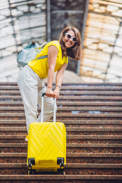 γυναίκα τραβώντας προς τα επάνω από σκάλες βαριά κίτρινη βαλίτσα με τροχούς έννοια ταξιδιού - Φωτογραφία, εικόνα