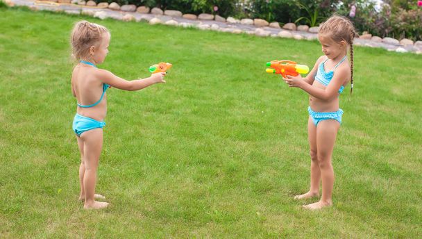 Дві маленькі чарівні дівчата грають з водяними гарматами у дворі
 - Фото, зображення