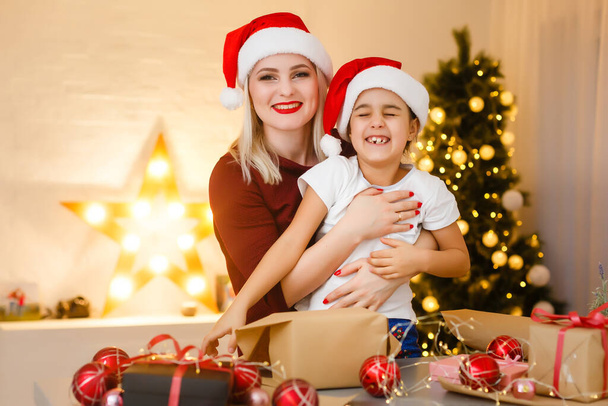 Hyvää joulua ja hyvää joulua. Äiti ja tytär valmistelevat joululahjoja. Baubles, lahjat, karkkia joulukoristeita.. Joulun perheen perinteet. - Valokuva, kuva