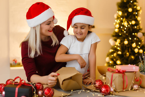 Frohe Weihnachten und frohe Feiertage. Mutter und Tochter bereiten Weihnachtsgeschenke vor. Kugeln, Geschenke, Süßigkeiten mit Weihnachtsschmuck.. Weihnachtliche Familientradition. - Foto, Bild