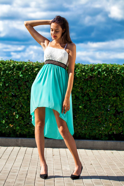 Full-length portrait of a young slender beautiful girl in a turquoise dress posing on the embankment - Foto, afbeelding