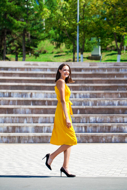 Full body portrait of a young beautiful brunette woman walking in summer street - Fotó, kép