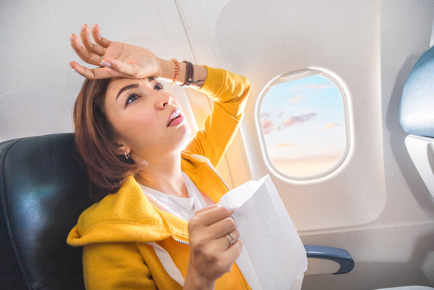 Una viajera asiática sufre un ataque agudo de náuseas durante la turbulencia en un avión. La mujer estaba mareada y airsock durante el vuelo aéreo - Foto, Imagen