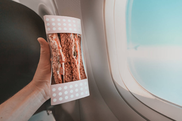 Sandwiches in hand in the cabin during the airplane flight. Concept of food in the economy segment - Valokuva, kuva