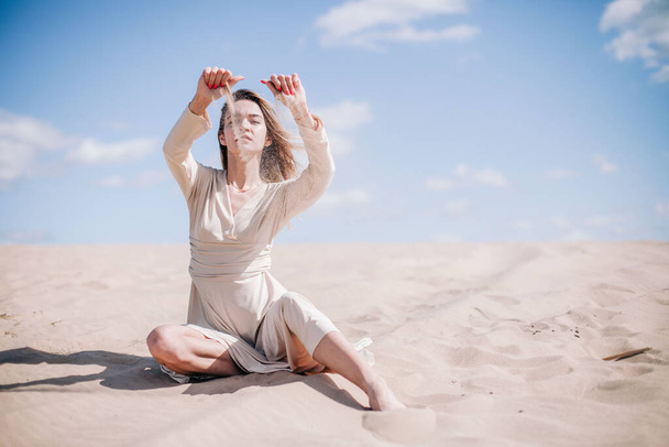 Ein junges, schlankes Mädchen in einem beigen Kleid posiert in der Wüste im Wind - Foto, Bild