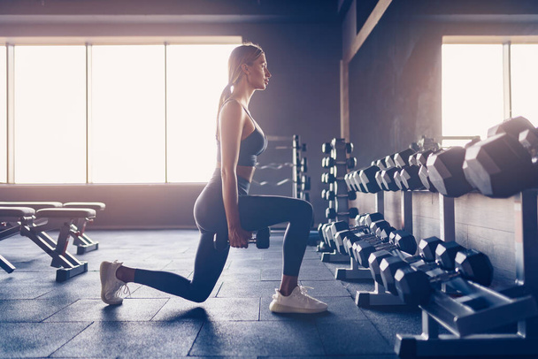 Beautiful girl doing lunges exercise with dumbbells in gym - Fotoğraf, Görsel
