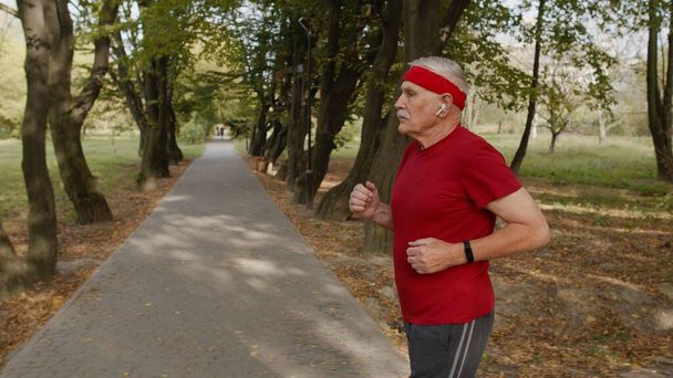 Zijaanzicht van bejaarde sportman training. Trainen cardio buiten in het stadspark 's morgens - Foto, afbeelding