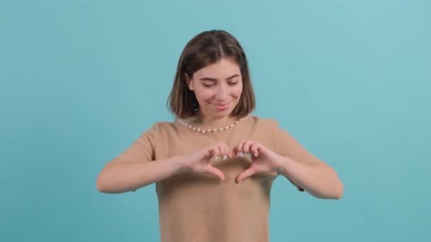 gelukkig vrouw gezet merk met vingers hart vorm, geïsoleerd op turquoise achtergrond. - Video