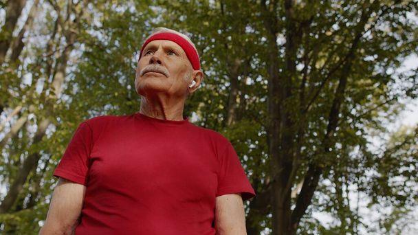 都会の公園で音楽を聴き健康的なアクティブなライフスタイルを楽しむシニア老人ランナー - 写真・画像