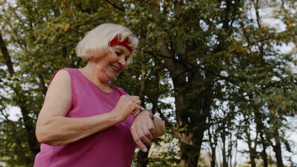 Starsza biegaczka sportowa używająca inteligentnego zegarka, dotykająca ekranu dotykowego, śledząca dystans, sprawdzająca puls - Zdjęcie, obraz