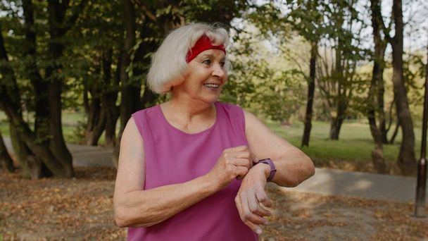 Senior mulher corredor esporte usando relógio inteligente tocando touchscreen, resultado de rastreamento. Exercício de fitness - Foto, Imagem