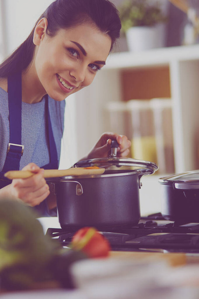 Mutfakta ahşap kaşıkla yemek pişiren kadın - Fotoğraf, Görsel
