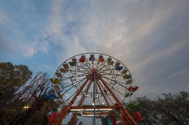 Вид снизу колеса обозрения в начале вечера под голубым небом на закате, пейзаж уличной фотографии - Фото, изображение