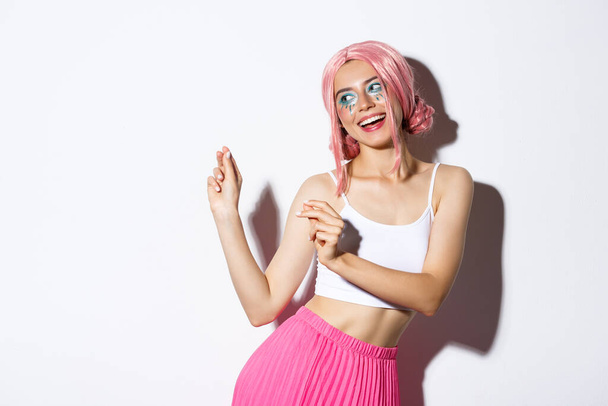 Image of attractive party girl with pink wig and bright makeup, having fun and celebrating holiday, dancing happy over white background - Fotografie, Obrázek