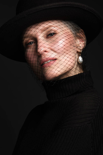 Portrait of a beautiful elderly woman in a black shirt with classic makeup and veil on the face. - Photo, Image