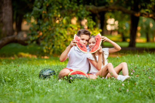boy and girl sit on the grass and eat juicy watermelon - Fotoğraf, Görsel