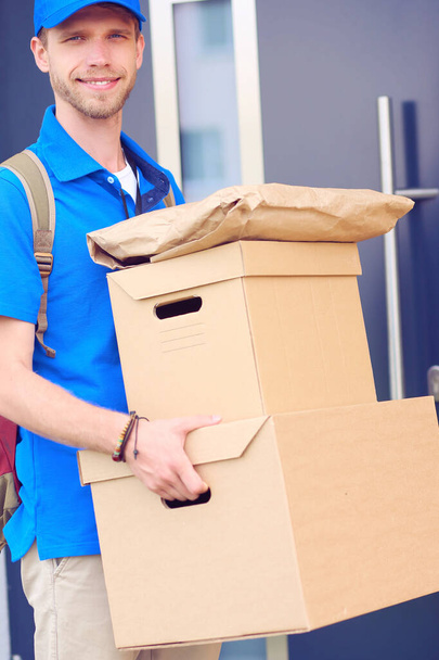 Smiling delivery man in blue uniform delivering parcel box to recipient - courier service concept - Фото, изображение