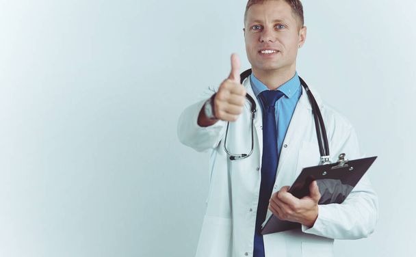 Portrait of handsome doctor in white coat holding a folder, showing Ok sign - Фото, изображение
