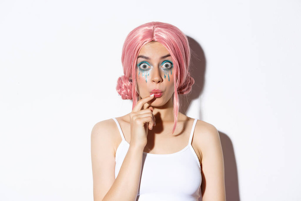 Крупный план глупой красивой девушки в розовом парике, смотрящей в камеру, стоящей на белом фоне - Фото, изображение