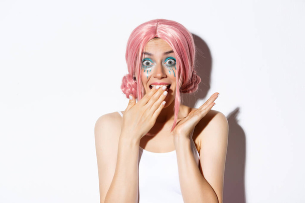 Крупный план удивленный гламурная девушка в розовом парике, задыхаясь и улыбаясь удивлен, стоя на белом фоне - Фото, изображение