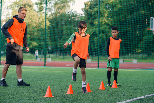 Concentrated junior soccer player running among orange cones that standing on artificial turf at stadium during workout - Fotoğraf, Görsel