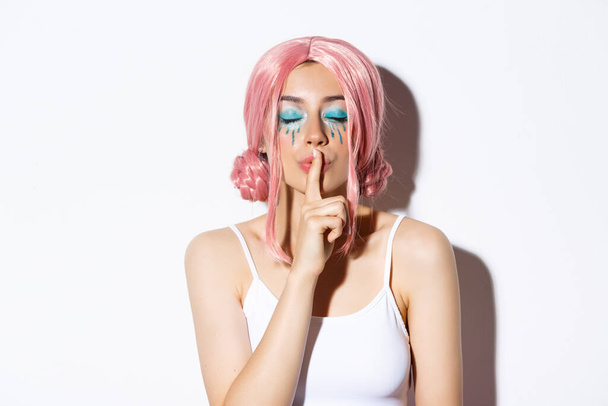 Close-up of lovely girl with pink wig and bright makeup, close eyes and shushing, have surprise or secret, standing over white background - Fotografie, Obrázek