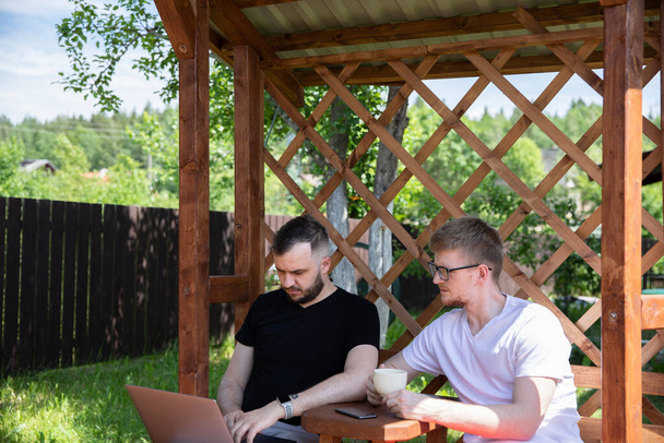 couple d'amis regardant ordinateur portable sur fond de grille de pergola en bois - Photo, image