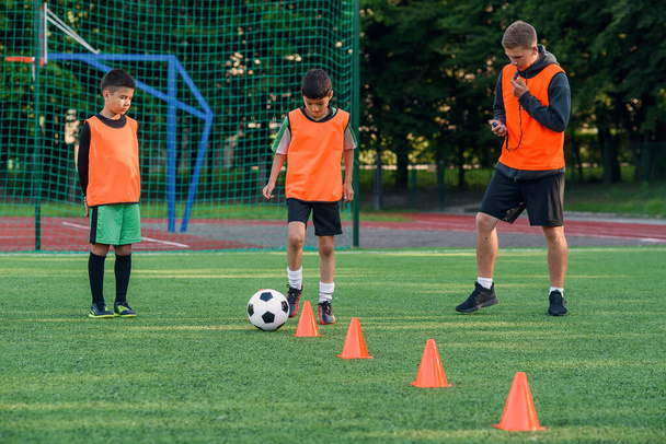 Persistent teen boy in sportswear trains football on soccer field and learns to circle the ball between training cones. - 写真・画像