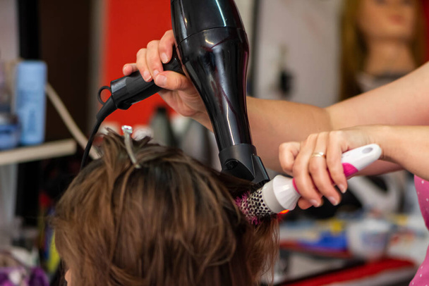 Beautiful teen girl at the hairdresser blow drying her hair after cutting it - 写真・画像