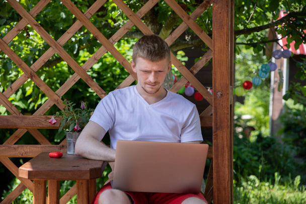 Νεαρός ελκυστικός επιχειρηματίας εργάζεται εξ αποστάσεως σε εξωτερικούς χώρους, κάνοντας σερφ με φορητό υπολογιστή - Φωτογραφία, εικόνα