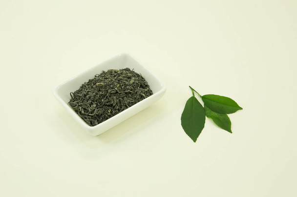 Kínai zöld tea. Zöld tea Pekingből. Citromlevél. Fehér tálban, fehér alapon elkülönítve. - Fotó, kép