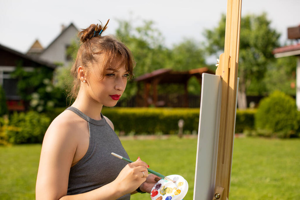 mooie meisje kunstenaar is schilderij met verf borstels als haarspelden in haar haar - Foto, afbeelding