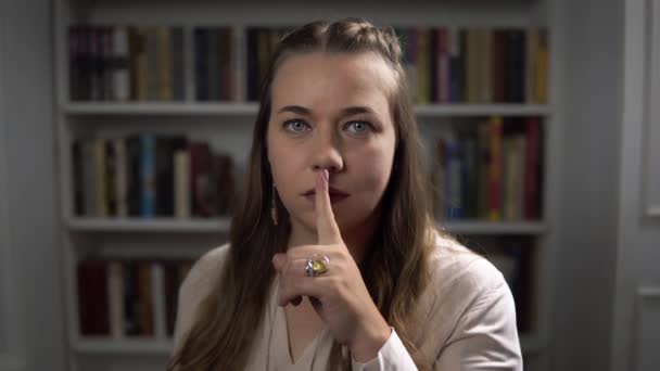 Nuori nainen sinisilmäinen laittaa sormensa huulille tehdä hiljaisuus - Materiaali, video