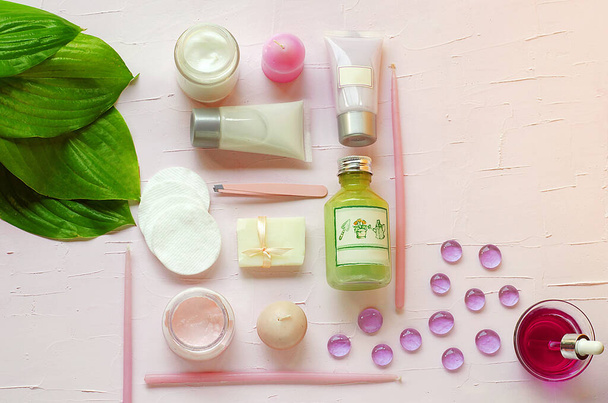 Green fresh leaves on the background of organic cosmetics. Towels, cotton pads, pink cream, green gel, candle soap. Natural cosmetics. SPA. Aromatherapy.Copy space. View from above. Flat view.Eyebrow - Foto, imagen