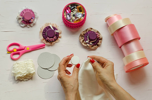 Stap 9. Op een witte tafel staan roze schaar, stof, sieraden, linten en haarspelden. Vrouwelijke handen doen ambachten worden afgebeeld.Met je eigen handen. Stap voor stap instructie. Doe het zelf. Ambacht voor het nieuwe jaar - Foto, afbeelding