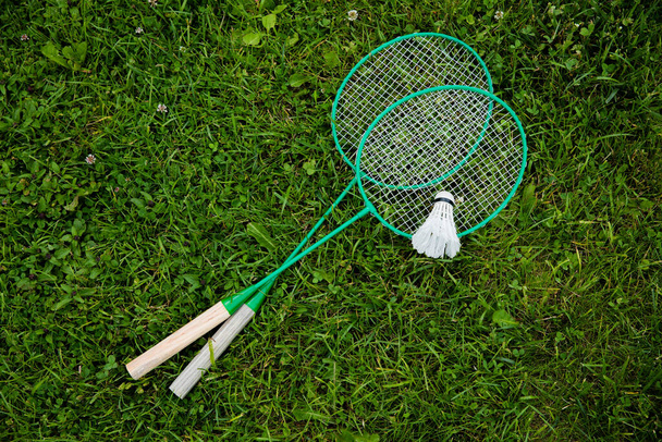 Badminton rackets and shuttlecock laying on green grass, outdoors game - Zdjęcie, obraz