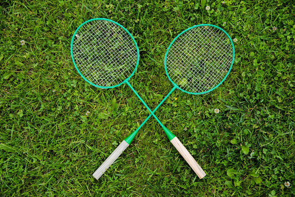 Badminton rackets laying on green grass crossed as x, outdoors, Copy text space - Foto, Imagem