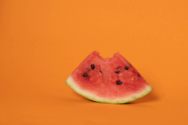 bitten slice of red watermelon on orange background - Фото, зображення