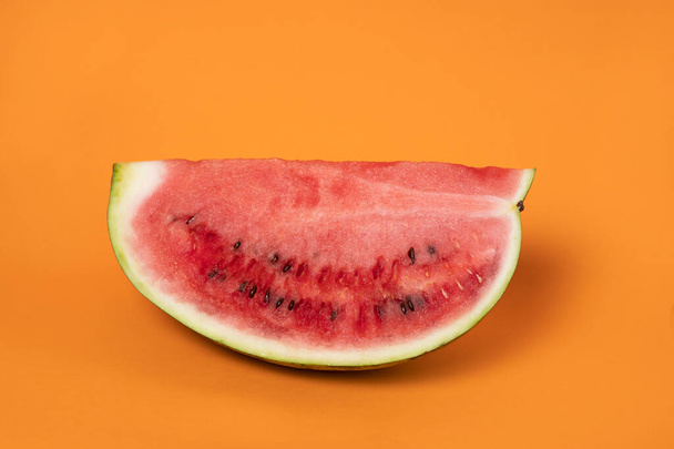 auf orangefarbenem Hintergrund liegt eine Wassermelone in einem Schliff - Foto, Bild