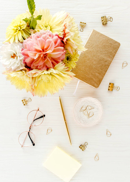 Flat lay womens office desk. Female workspace with yellow dahlias and roses flowers, accessories, golden diary, white wooden background. Top view. - Foto, immagini