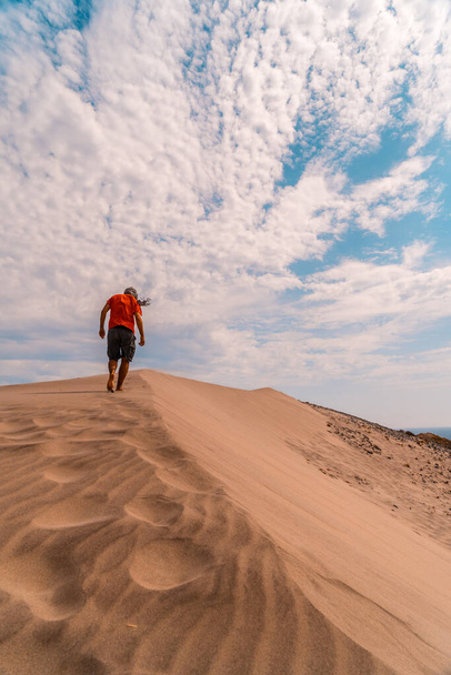 A man with a red shirt and a turban on his head, walking in the desert of the dune of Playa de Mnsul in the natural park of Cabo de Gata, Nijar, Andalucia. Spain, Mediterranean Sea - Foto, imagen