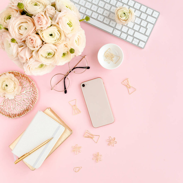 Stylized, pink womens home office desk. Workspace with computer, bouquet ranunculus and roses, phone on pink background. Flat lay. Top view. - Photo, image