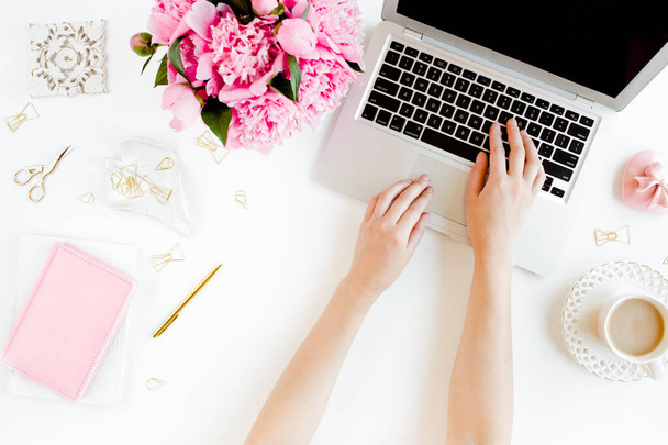 Female workspace with female hands, laptop, pink peonies bouquet, accessories on white background. Top view feminine background. Flat lay. - Foto, Imagem