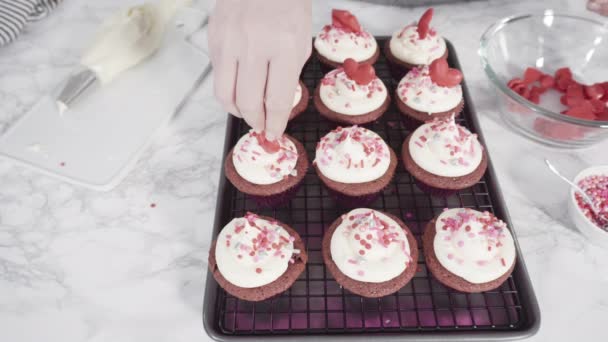 Rote Samt-Cupcakes mit rosa italienischem Buttercreme-Zuckerguss und dekoriert mit herzförmigen und kussförmigen roten Pralinen. - Filmmaterial, Video